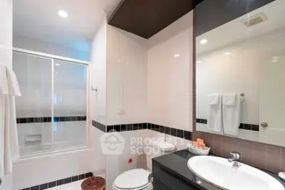 Modern bathroom with sleek black and white tiles, glass shower door, and elegant fixtures.