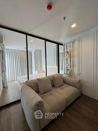 Modern bedroom with glass partition and cozy sofa, featuring elegant decor and natural light.