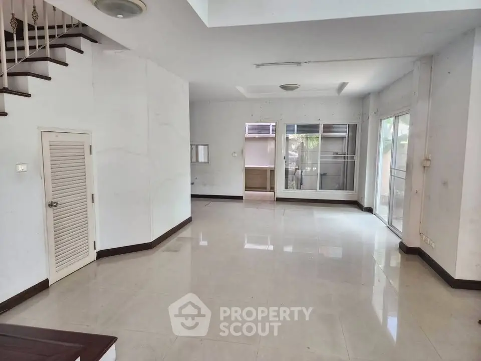 Spacious empty living room with large windows and staircase, ideal for customization.