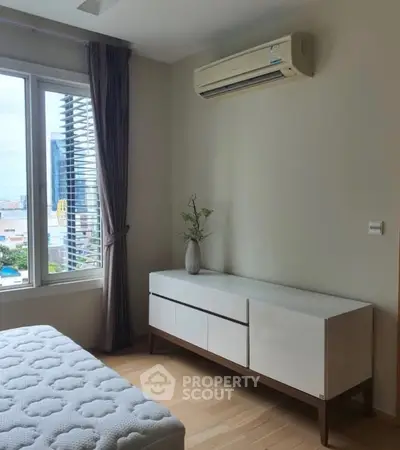 Modern bedroom with large window and air conditioning, featuring a sleek white dresser and wooden flooring.