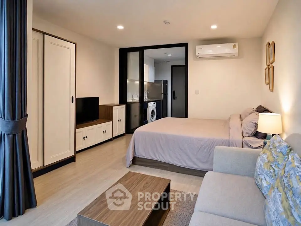 Modern studio apartment with cozy living area and compact kitchen featuring washing machine.