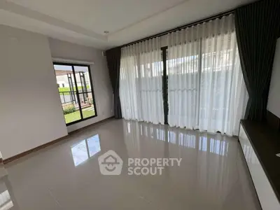 Spacious living room with large windows and elegant curtains, offering ample natural light and modern design.