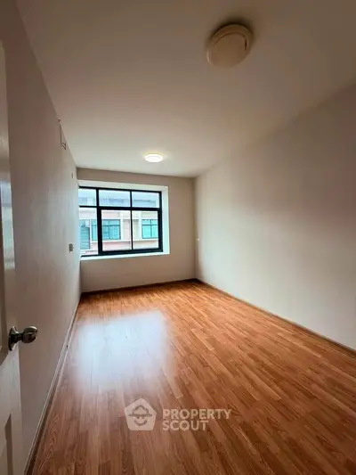 Spacious empty room with wooden flooring and large window, perfect for customization.
