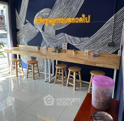 Modern cafe interior with stylish wooden counter and stools, featuring unique wall art and bright lighting.