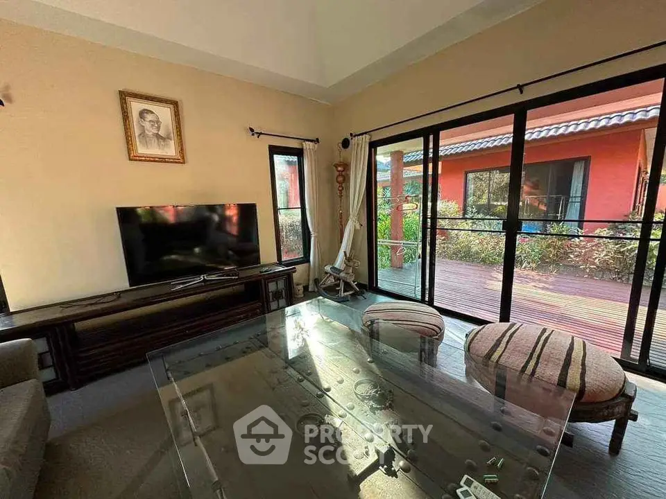 Cozy living room with glass table and TV, opening to a sunny patio with garden view.