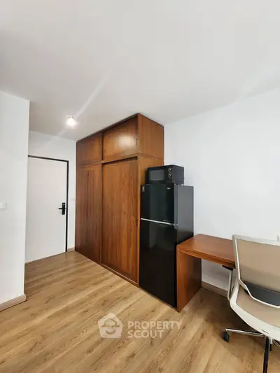 Modern apartment interior with wooden flooring, built-in wardrobe, and compact fridge in a study area.