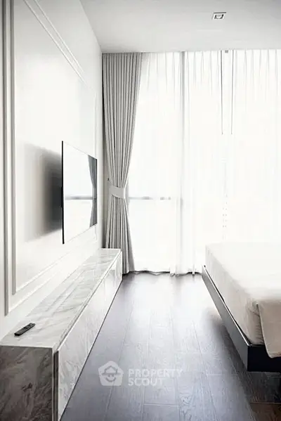 Modern bedroom with sleek TV setup and floor-to-ceiling windows for natural light.