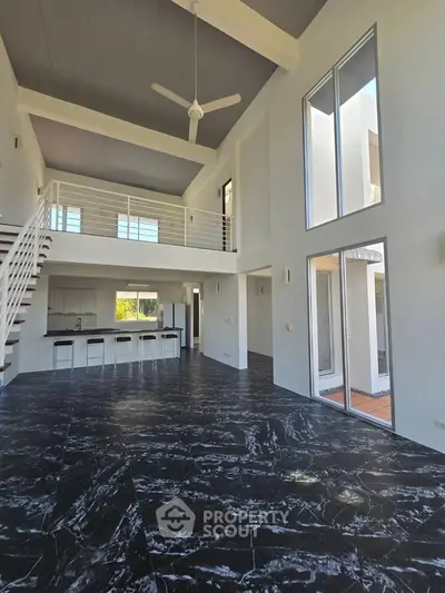 Spacious modern living room with high ceilings and mezzanine, featuring sleek black marble flooring.