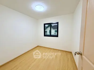 Spacious empty bedroom with wooden flooring and a window view, perfect for customization.