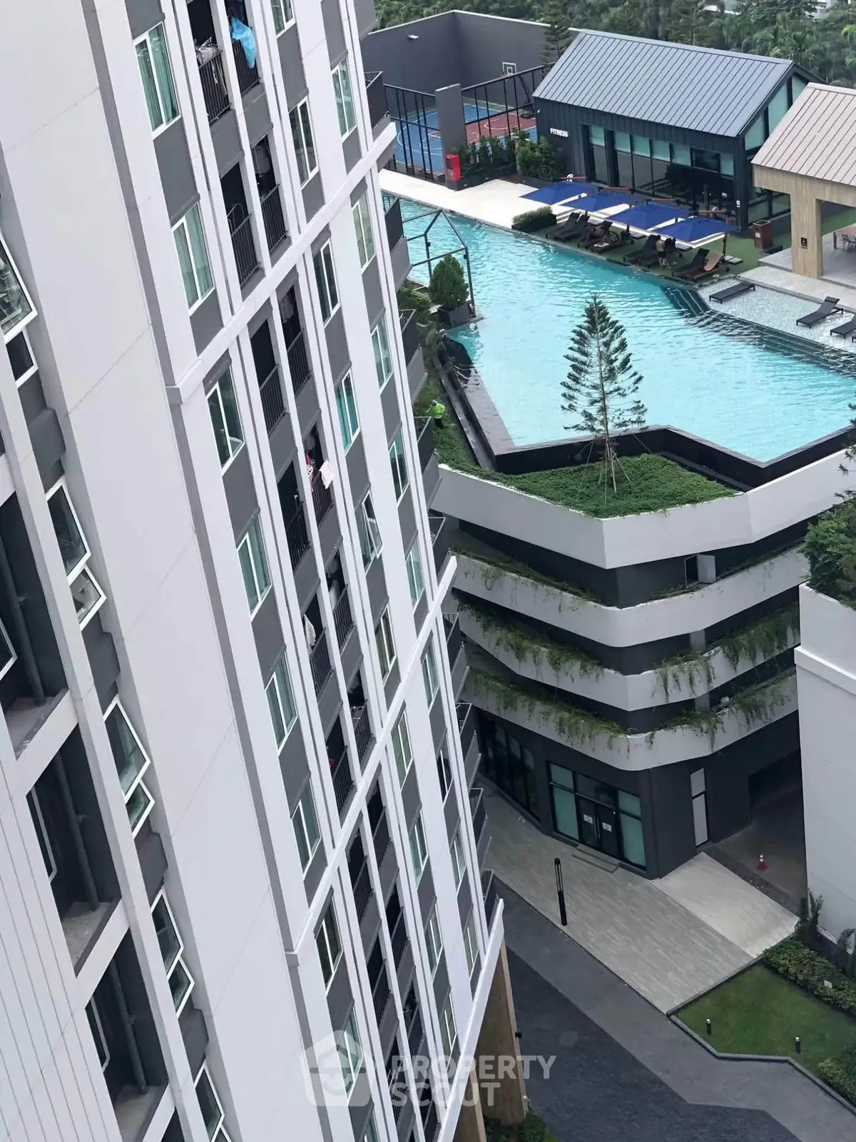 Modern high-rise building with rooftop pool and lush greenery, offering luxurious urban living.
