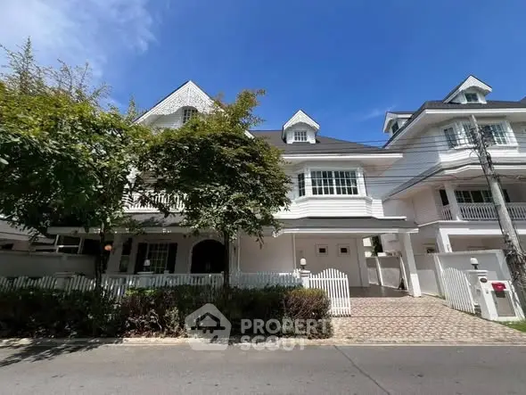 Charming white townhouse with lush greenery and spacious driveway under a clear blue sky.