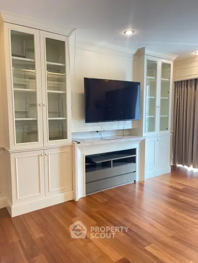 Spacious living room with built-in cabinets and mounted TV, featuring elegant hardwood floors.