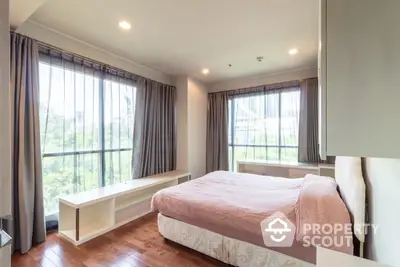 Spacious bedroom with large windows offering ample natural light and a serene view, complemented by elegant curtains and hardwood flooring.