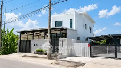 Modern two-story house with sleek design and gated entrance under a clear blue sky.
