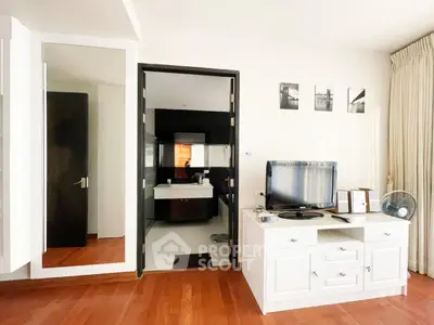 Modern living room with wooden flooring and stylish decor, featuring a TV unit and a glimpse into a sleek bathroom.
