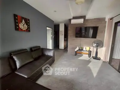 Modern living room with sleek black leather sofa and wall-mounted TV, featuring stylish decor and ample natural light.