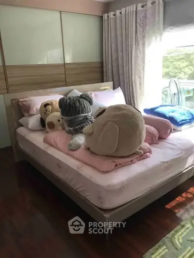 Cozy bedroom with plush toys on a neatly made bed, featuring large windows and elegant curtains.