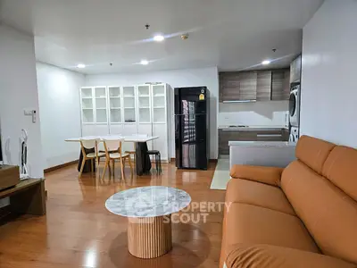 Modern open-plan living room with kitchen, featuring sleek furniture and hardwood floors.