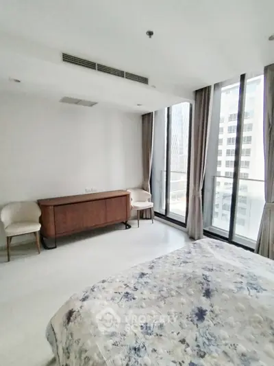 Spacious bedroom with large windows offering city views in modern apartment.