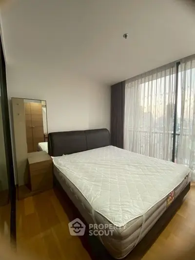 Spacious bedroom with large window and city view, featuring a comfortable bed and wooden flooring.