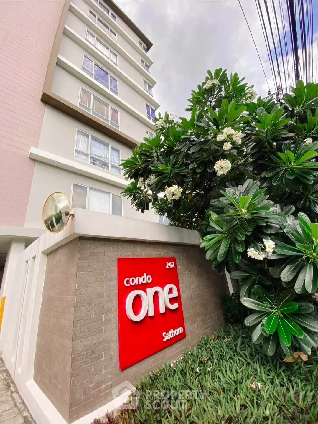 Modern condo building exterior with lush greenery and prominent signage.