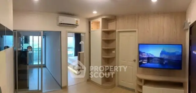 Modern living room with built-in shelves and flat-screen TV, leading to a bright bedroom with balcony view.