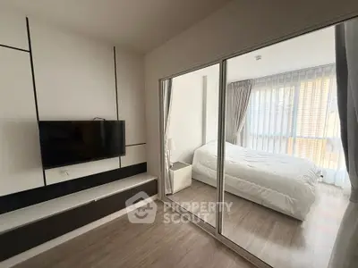 Modern bedroom with glass partition and mounted TV, featuring sleek design and natural light.