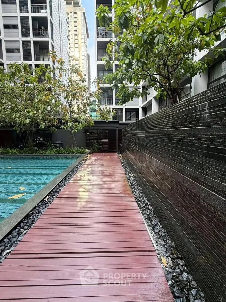 Modern apartment complex with poolside walkway and lush greenery.