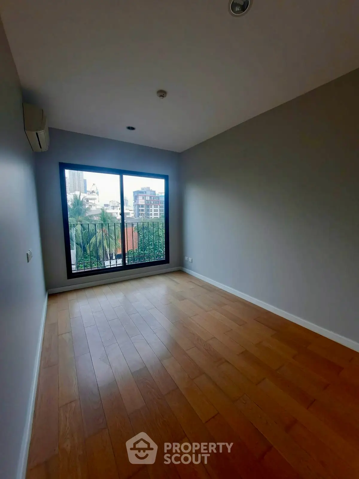 Spacious bedroom with wooden flooring and large window offering city views.