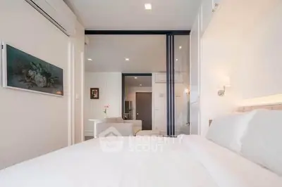 Modern bedroom with white decor and sliding glass doors leading to a cozy living area.