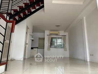 Spacious open-plan living area with staircase and tiled flooring, featuring a compact kitchen and air conditioning.