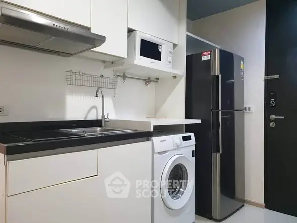 Modern kitchen with sleek appliances including washing machine and fridge in compact layout.