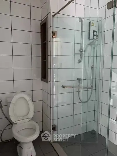 Modern bathroom with glass shower enclosure and white tiled walls.