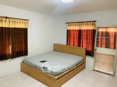 Spacious bedroom with large windows and natural light, featuring a modern bed frame and tiled flooring.
