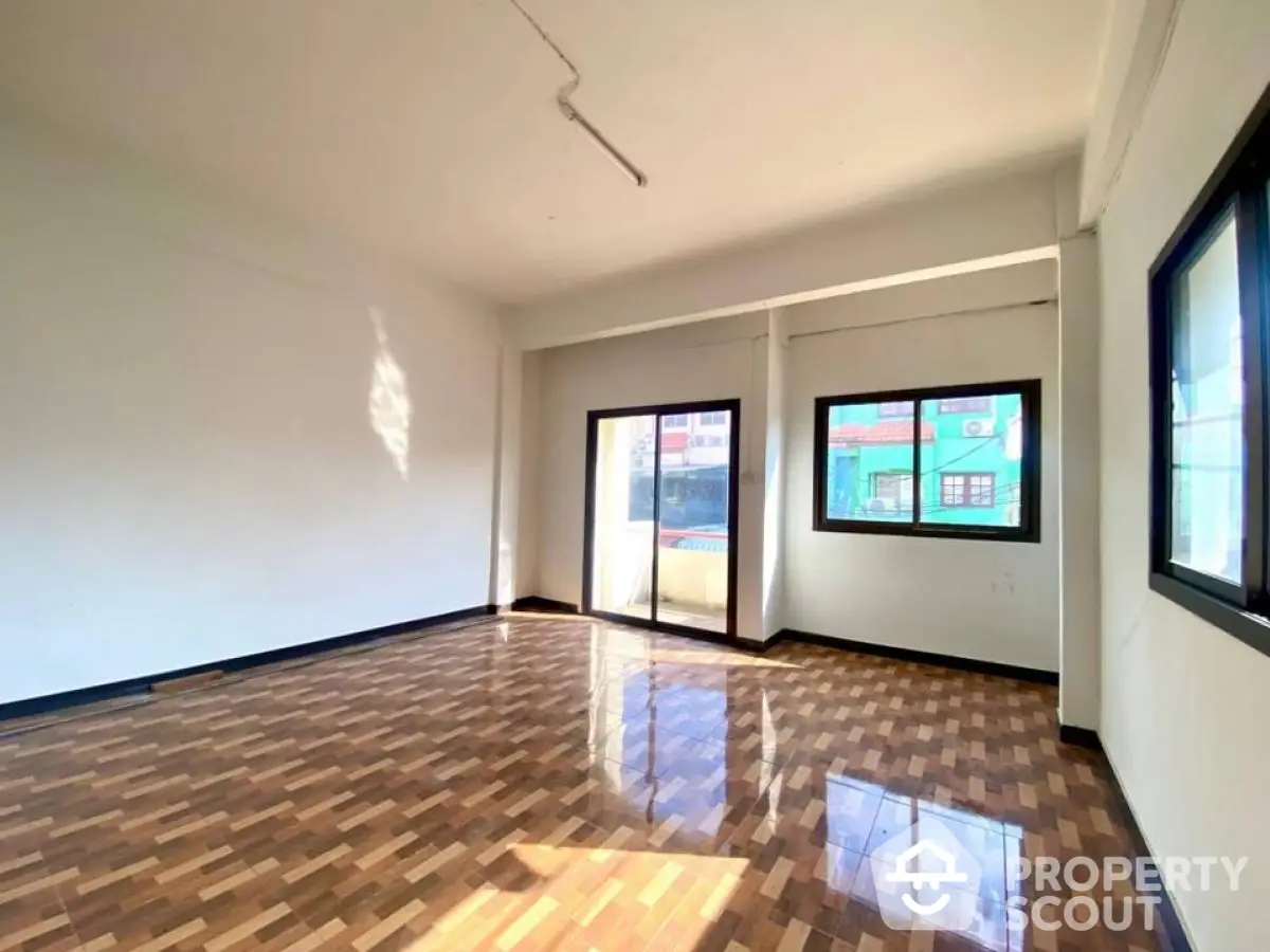 Spacious sunlit room with wooden flooring and large windows