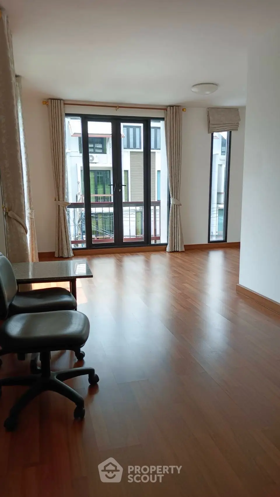 Spacious room with wooden flooring and large windows offering ample natural light.