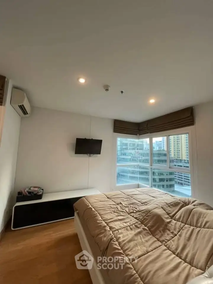 Modern bedroom with city view, featuring a cozy bed, wall-mounted TV, and large windows for natural light.