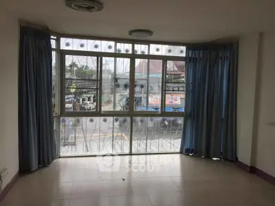 Spacious room with large windows and blue curtains offering a street view, ideal for natural light lovers.