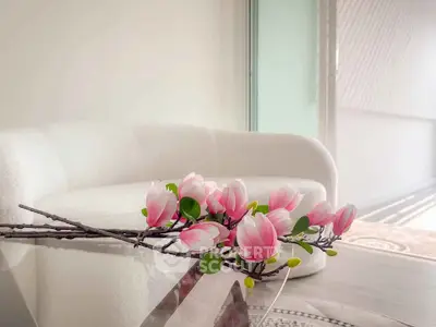 Elegant modern living room with white sofa and glass table adorned with pink flowers, bathed in natural light.
