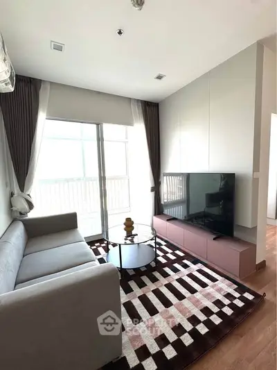 Modern living room with stylish decor, large TV, and natural light from balcony.