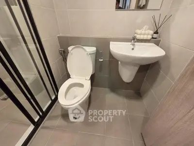 Modern bathroom with sleek fixtures and neutral tiles, featuring a shower and contemporary sink.