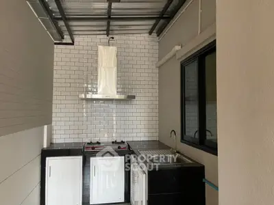 Compact urban kitchen with modern gas stove, stainless steel sink, and white subway tile backsplash, featuring exposed ceiling pipes for an industrial vibe.