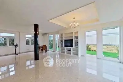 Spacious living room with elegant chandelier and built-in TV unit, featuring large windows and glossy flooring.
