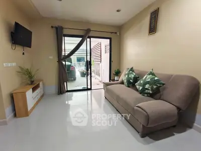 Cozy living room with modern sofa and wall-mounted TV, leading to a small outdoor area.