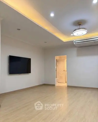 Spacious modern living room with wooden flooring and ceiling lights, featuring a wall-mounted TV and air conditioning.