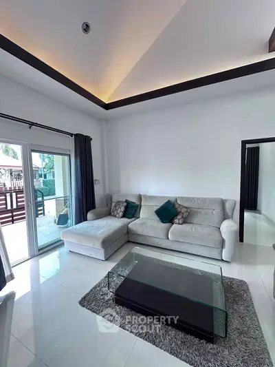 Spacious living room with modern sofa and glass coffee table, featuring large windows and balcony access.
