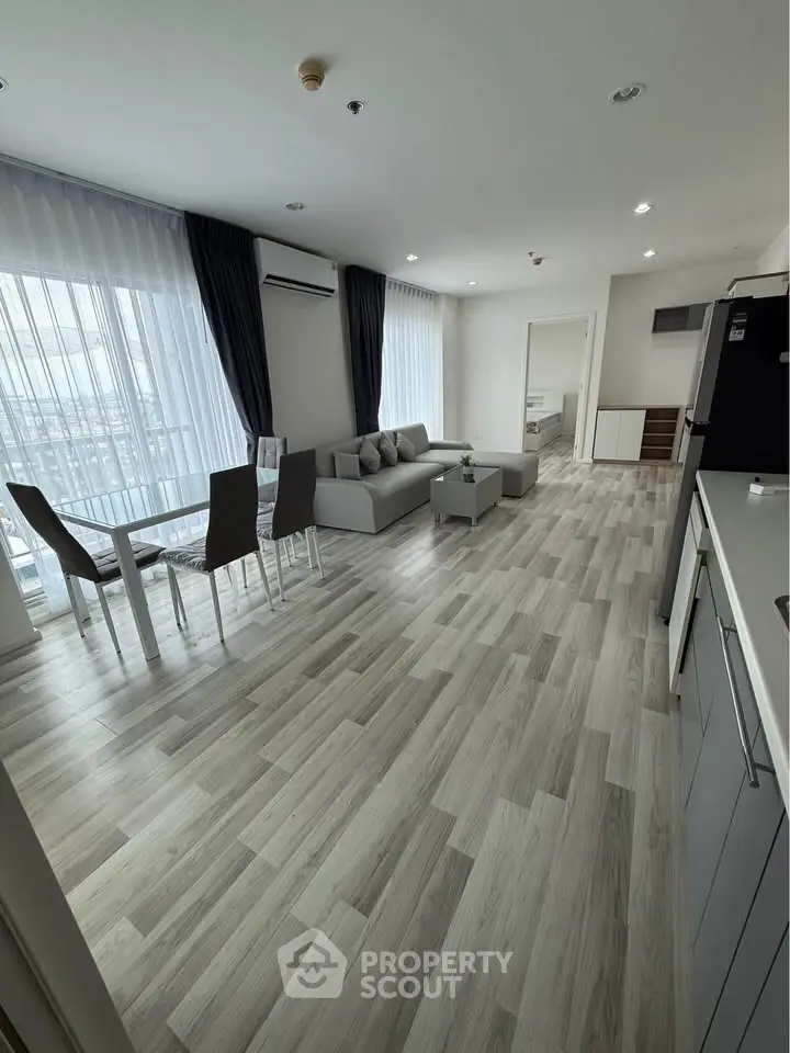 Spacious modern living room with open kitchen and elegant dining area, featuring sleek flooring and ample natural light.