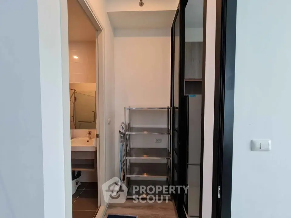 Modern apartment entryway with bathroom and storage area, featuring sleek shelving and contemporary design.