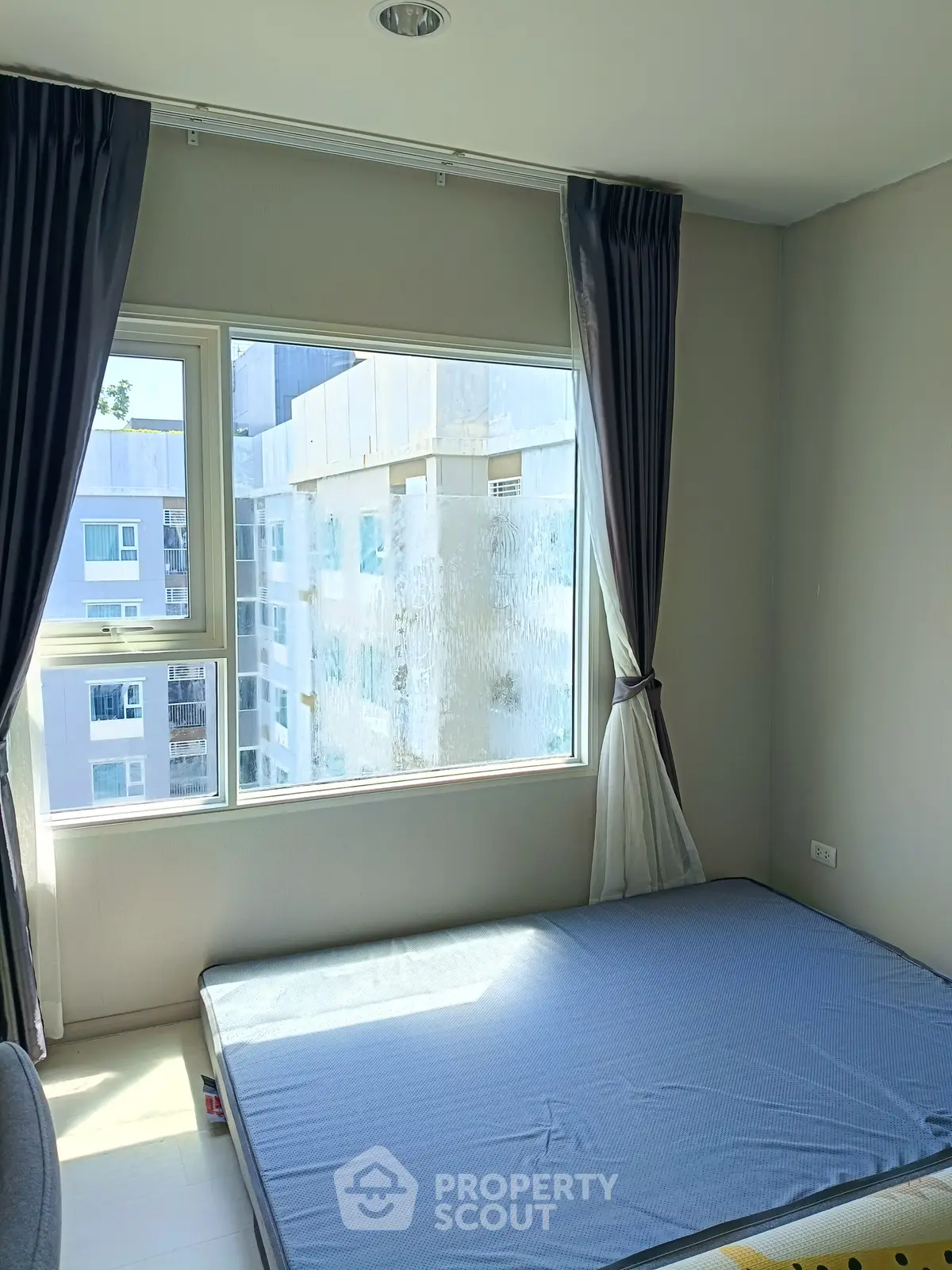 Bright bedroom with large window and city view, featuring minimalist decor and natural light.