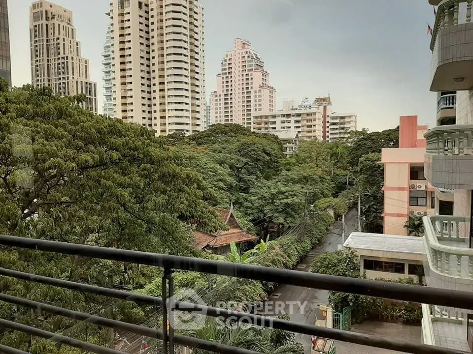 Stunning urban view from balcony overlooking lush greenery and modern high-rise buildings.